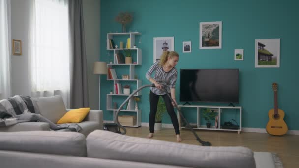 Wide shot of young beautiful girl vacuuming her cozy apartment - Video