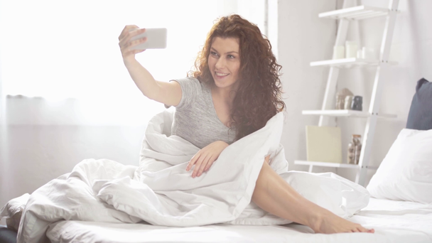 bella ragazza avendo video chat su smartphone, agitando e sorridendo a letto
  - Filmati, video