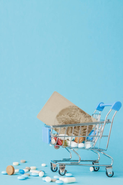 Pills and credit card in shopping trolley on blue background. Creative idea for health care cost, drugstore, health insurance and pharmaceutical company business concept. Copy space - Photo, image