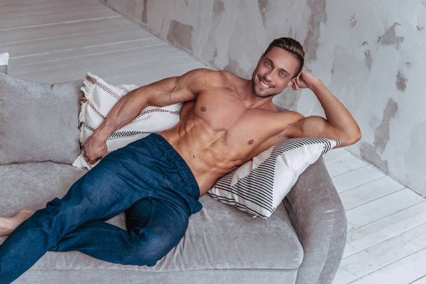 Portrait of strong healthy handsome athletic man. Fitness model posing and smiling while lying on the sofa. Fitness lifestyle concept - Фото, зображення