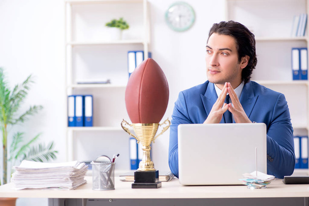 Joven hombre de negocios guapo con pelota de rugby en la oficina
 - Foto, Imagen