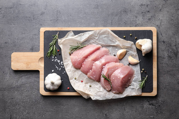 Board with cut raw turkey fillet and ingredients on grey background, top view - Foto, immagini