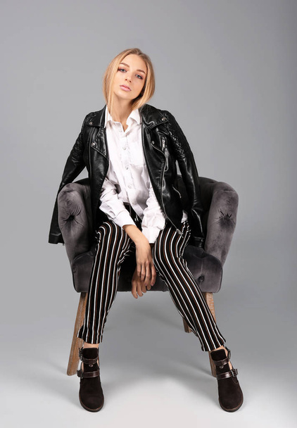 Young stylish woman with trendy shoes sitting in armchair on grey background - Foto, immagini