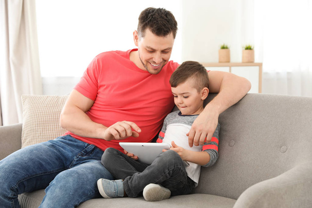 Boy and his father with tablet sitting on sofa at home. Family time - Foto, immagini