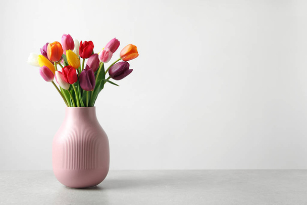 Vase with beautiful spring flowers on table against light background, space for text - Foto, Imagen