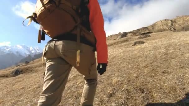 Gelukkige reiziger meisje fotograaf in zonnebril met een camera en een rugzak gaat bergopwaarts op een achtergrond van besneeuwde toppen op een zonnige dag - Video