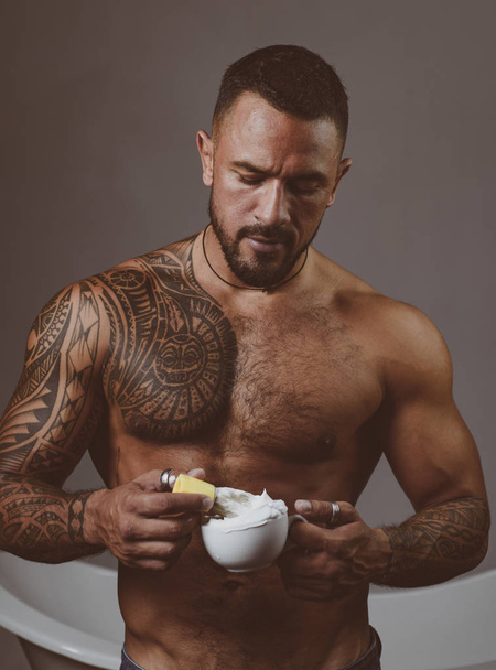Shaving with a real blade sounds cool. Muscular latino man preparing shaving cream. Handsome hispanic guy holding shaving brush in strong hands. Bearded man going to shaving his facial hair - Photo, image