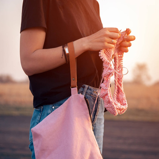 Photo de style de vie atmosphérique extérieur de jeune belle femme aux cheveux foncés souriant et tricotant avec crochet de tricot à partir d'un fil de laine naturel une sueur rose
 - Photo, image