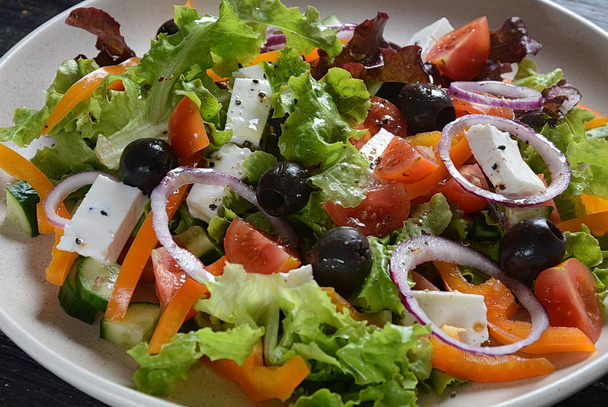 新鮮なキュウリ、チェリートマト、甘いコショウ、レタス、赤玉ねぎ、オリーブ、オリーブオイルを暗い木製の素朴な背景に持つギリシャのサラダ。健康食品のコンセプト - 写真・画像