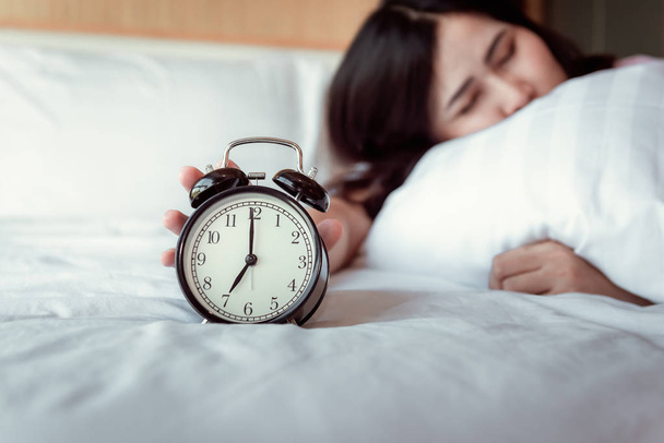 Turning off Sound or Snoozing The Alarm Clock Concept, Beautiful Woman Waking Up in The Morning at Bedroom While Her Hand is extending Alarm of Timer Clock. - Photo, Image