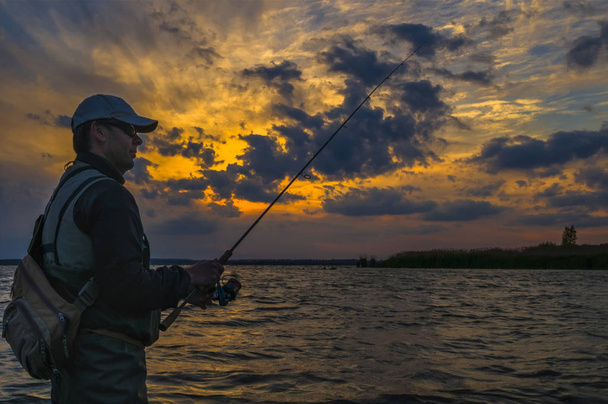 Silueta rybář. Muž ve vodě s rybářským tyčkou na pozadí oblačné situace ve slunci - Fotografie, Obrázek