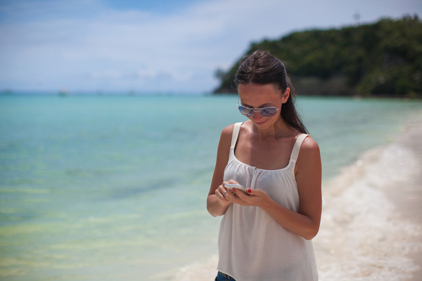 Nuori kaunis nainen rannalla etsii puhelimellaan
 - Valokuva, kuva