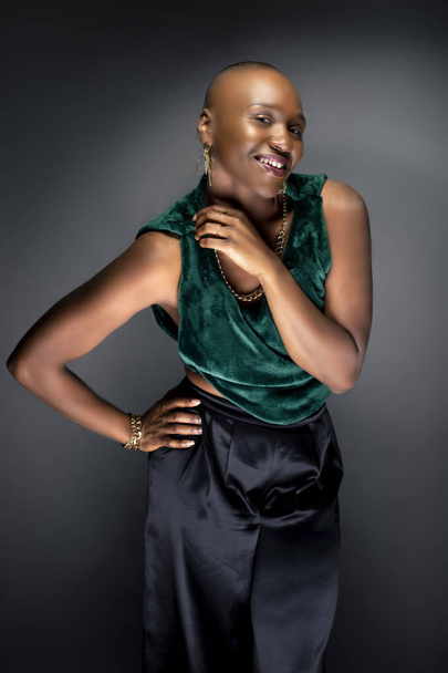 Black African American female fashion model posing with bald hairstyle and green trendy clothing.  Her bold modern look and muscular and fit body represents a strong and confident woman.   - Φωτογραφία, εικόνα