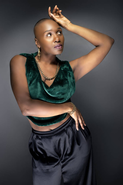 Black African American female fashion model posing with bald hairstyle and green trendy clothing.  Her bold modern look and muscular and fit body represents a strong and confident woman.   - Foto, Imagem