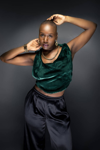 Black African American female fashion model posing with bald hairstyle and green trendy clothing.  Her bold modern look and muscular and fit body represents a strong and confident woman.   - Фото, изображение