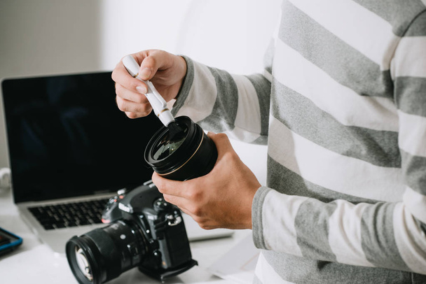 αρσενικό φωτογράφο κρατώντας ψηφιακή φωτογραφική μηχανή πάνω από το γραφείο στο φωτογραφικό του στούντιο - Φωτογραφία, εικόνα