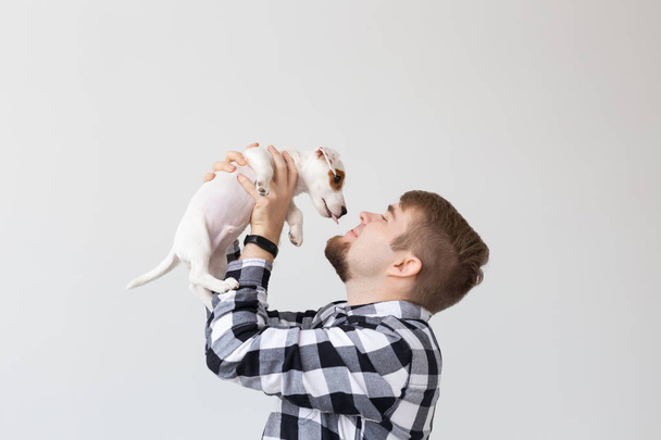 ανθρώπους, τα κατοικίδια ζώα και τα ζώα σύλληψη - νέος άνθρωπος που κρατά Τζακ Ράσελ τεριέ κουτάβι σε λευκό φόντο - Φωτογραφία, εικόνα