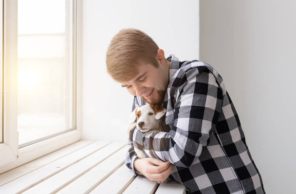 Άνθρωποι, κατοικίδιο και σκυλί ιδέα-νεαρός άντρας πάνω από το παράθυρο κρατώντας το κουτάβι Τζακ Ράσελ τεριέ - Φωτογραφία, εικόνα