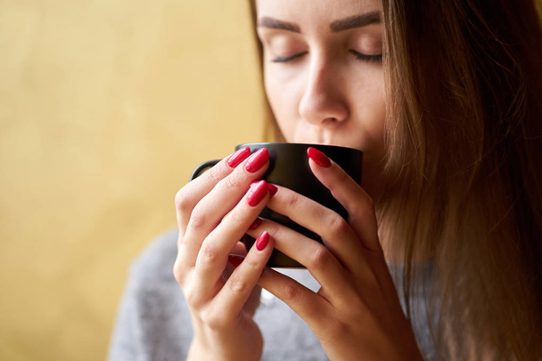 Beautiful girl with red nails holding a cup of coffee. Closeup v - Photo, image