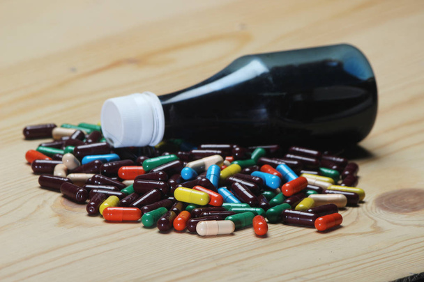 Closeup de pílulas de cápsulas coloridas ayurvédicas e uma garrafa de vidro cheia de líquido azul no fundo de madeira
. - Foto, Imagem