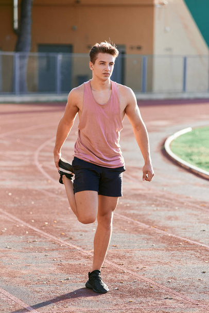 Young man runner stretching his leg on race track in stadium - Foto, Bild