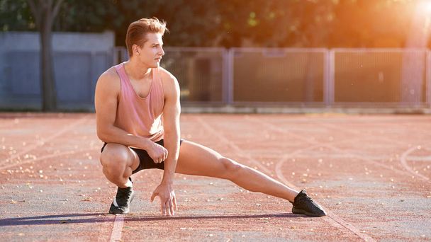 Young man runner stretching his leg on race track in stadium - Fotó, kép