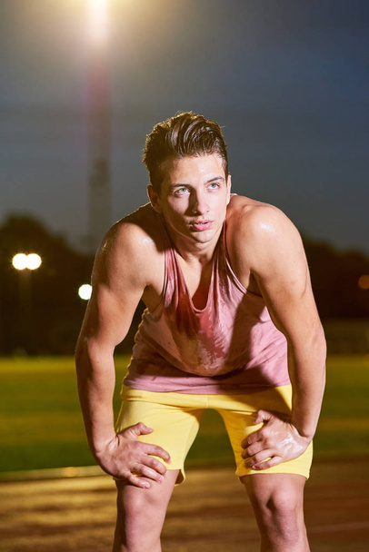 Portrait of a young muscular sweat sportsman posing on stadium - Photo, image