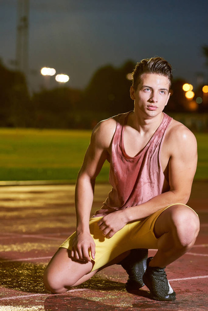 Portrait of a young muscular sweat sportsman posing on stadium - Фото, изображение