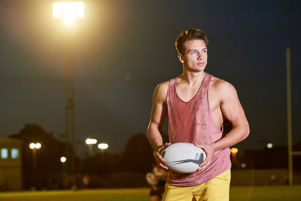 Young sweat American football player posing with a ball on the stadium - Фото, изображение