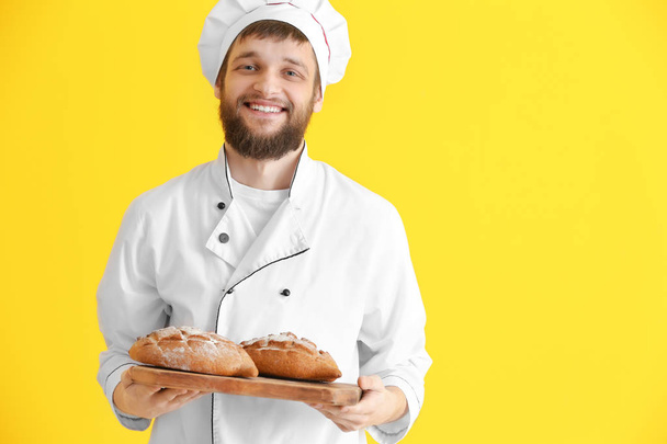 Young baker with fresh bread on color background - Fotoğraf, Görsel