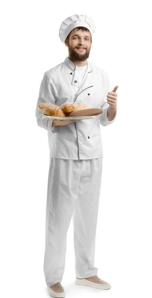Young chef with fresh bakery products showing thumb-up gesture on white background - Фото, зображення