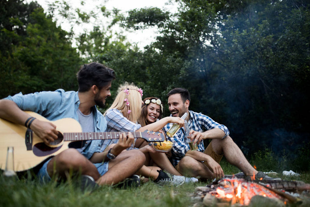 Happy friends playing music and enjoying bonfire in nature - Фото, зображення