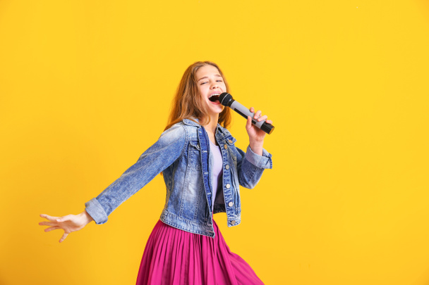 Mladá dívka s mikrofonem zpívající proti barevnému pozadí - Fotografie, Obrázek