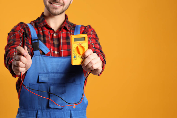 Electricista masculino con multímetro sobre fondo de color
 - Foto, imagen