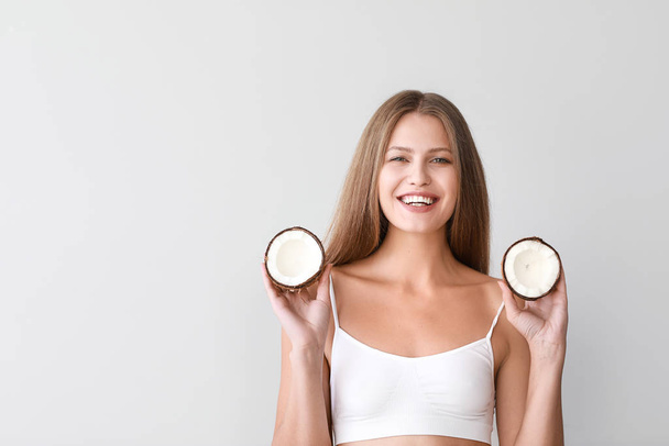 Mooie jonge vrouw met kokosnoot op lichte achtergrond - Foto, afbeelding
