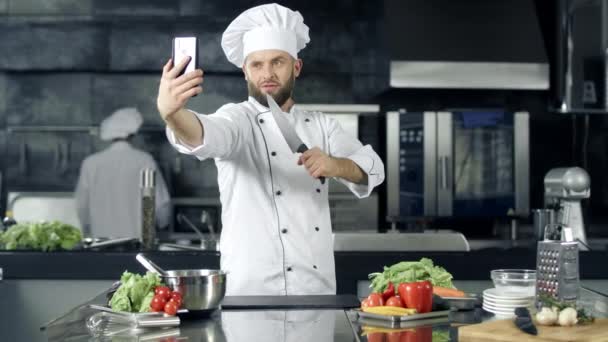Chef haciendo fotos en la cocina. Chef con cuchillo tomando selfie en el teléfono móvil
. - Imágenes, Vídeo