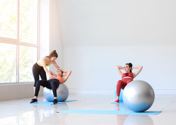 Jeunes femmes sportives avec des ballons de fitness faisant des exercices sous la supervision d'un entraîneur dans une salle de gym
 - Photo, image