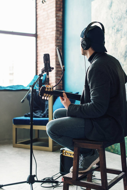 Κοντά σε έναν τραγουδιστή που κάθεται σε ένα σκαμνί σε ένα ακουστικό με μια κιθάρα που καταγράφει ένα κομμάτι σε ένα σπίτι στούντιο - Φωτογραφία, εικόνα