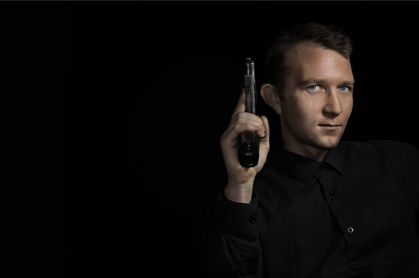 jovem homem close up retrato, no fundo preto com pistola
 - Foto, Imagem