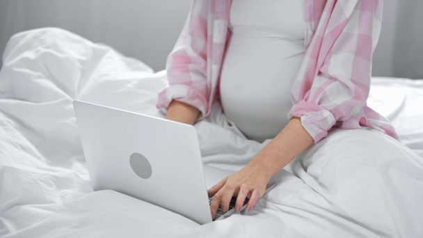 обрезанный вид беременной девушки с помощью ноутбука в постели
  - Кадры, видео