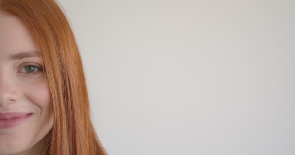 Half face portrait of beautiful ginger model watching smilingly and intently into camera on white background. - Footage, Video