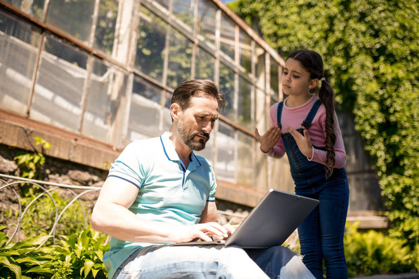 Daughter Is Trying To Draw Fathers Attention While Standing Outdoors.Father Is Typing On His Laptop. - Fotografie, Obrázek
