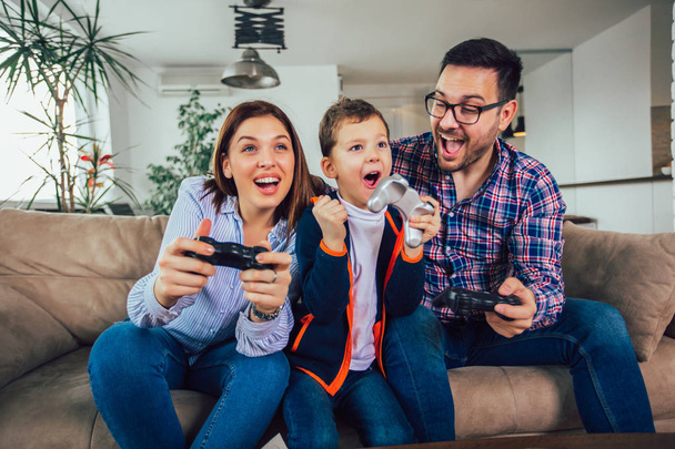 glückliche Familie sitzt auf einem Sofa und spielt Videospiele und isst - Foto, Bild