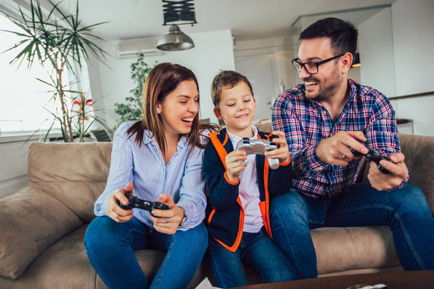 Ευτυχισμένη οικογένεια κάθεται σε έναν καναπέ και παίζοντας βιντεοπαιχνίδια και τ - Φωτογραφία, εικόνα