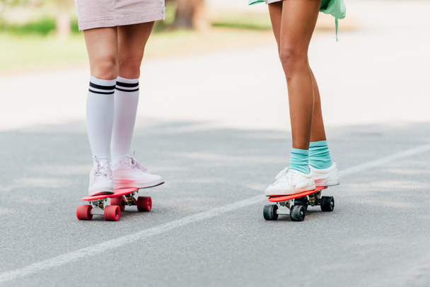partial view of two girls skateboarding on penny boards on road - Foto, imagen