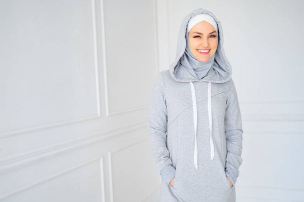 Πορτραίτο της νεαρής μουσουλμανικής γυναίκας με γκρι χιτζάμπ και εθνικό φόρεμα γυμναστικής στο σπίτι. - Φωτογραφία, εικόνα