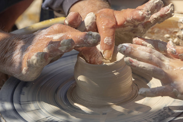 Dorosły Potter pomaga młodemu uczniowi zrobić gliniany garnek. Wytwarzanie na wolnym powietrzu na kole garnerów. Nauka rzemiosła - Zdjęcie, obraz