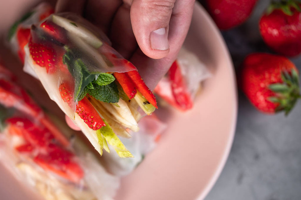 Close view of man holding fruity spring roll over plate with rolls on concrete table - Foto, Imagem