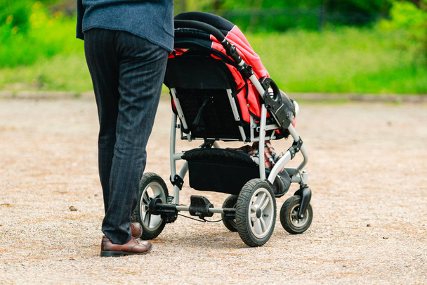 Chodzenie ojciec w kostiumie z wózkiem dla niemowląt na ulicy.  - Zdjęcie, obraz