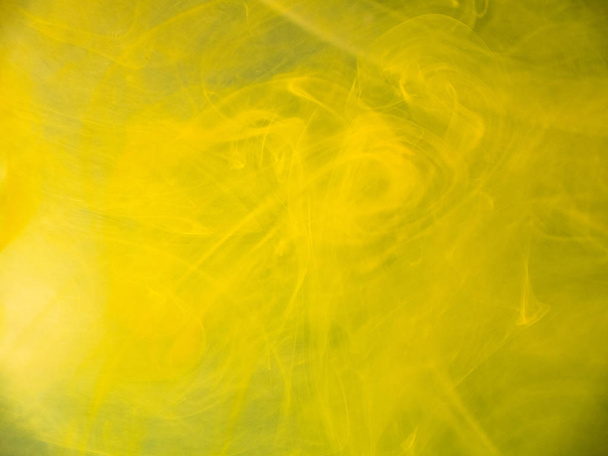 Yellow abstract smoke under water, blurred background. Close up view. Yellow paint dropped into water, abstract pattern. Paint dissolving into liquid, abstract background. Ink mixing with liquid. - Photo, image
